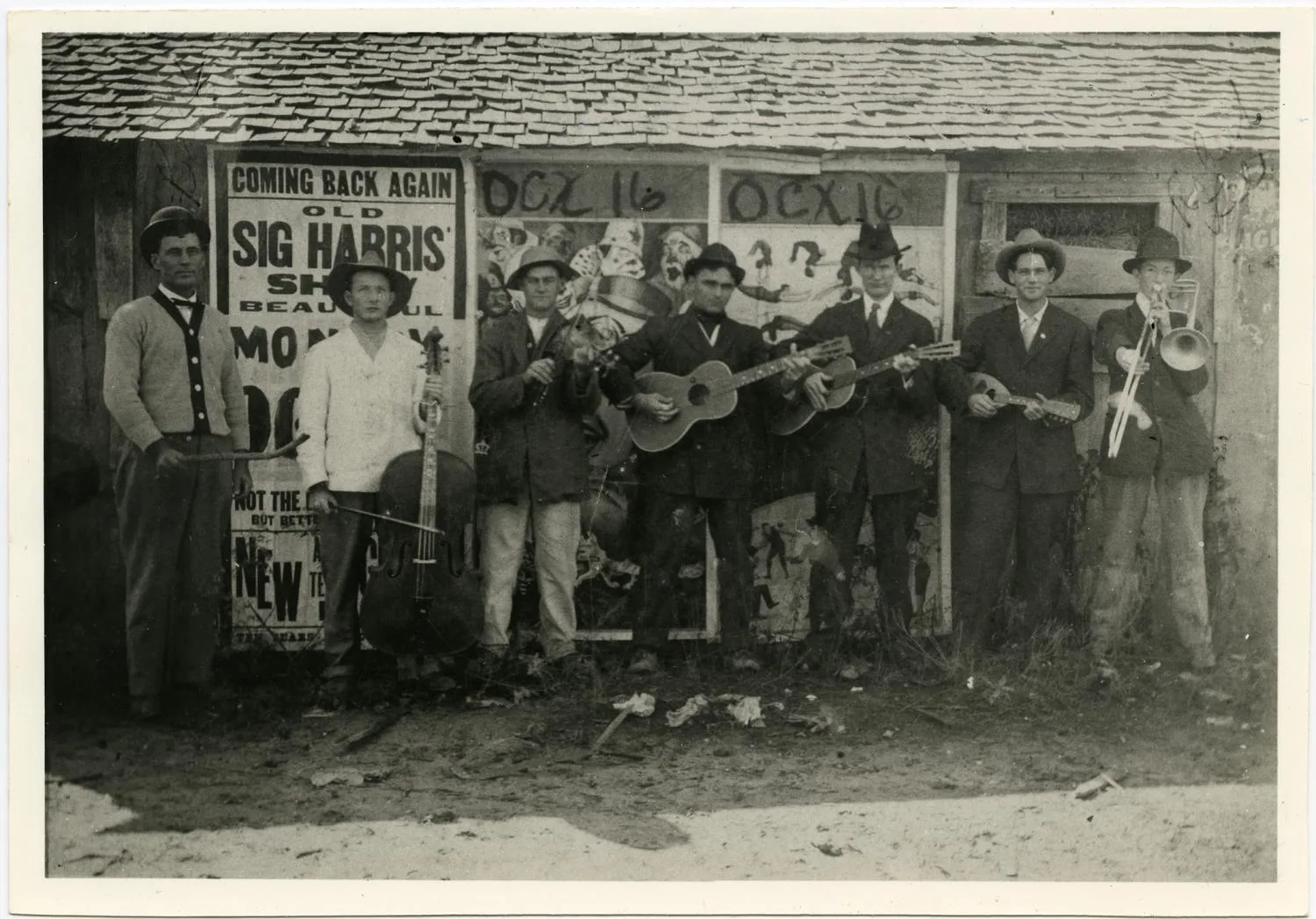 Photograph of Larry Taylor Band with seven members standing outside with their instruments. The wall behind them has large posters advertising entertainment.