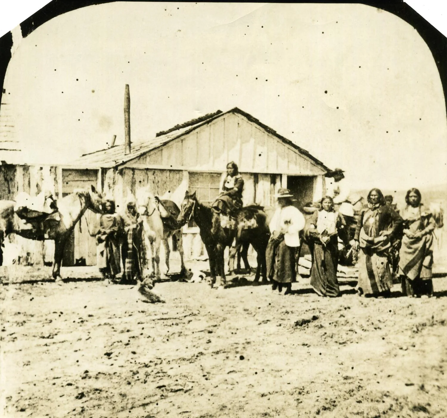 Photograph of part of Satanta's band of Kiowa with horses outside a sutler's store at the Kiowa Agency at Fort Sill.