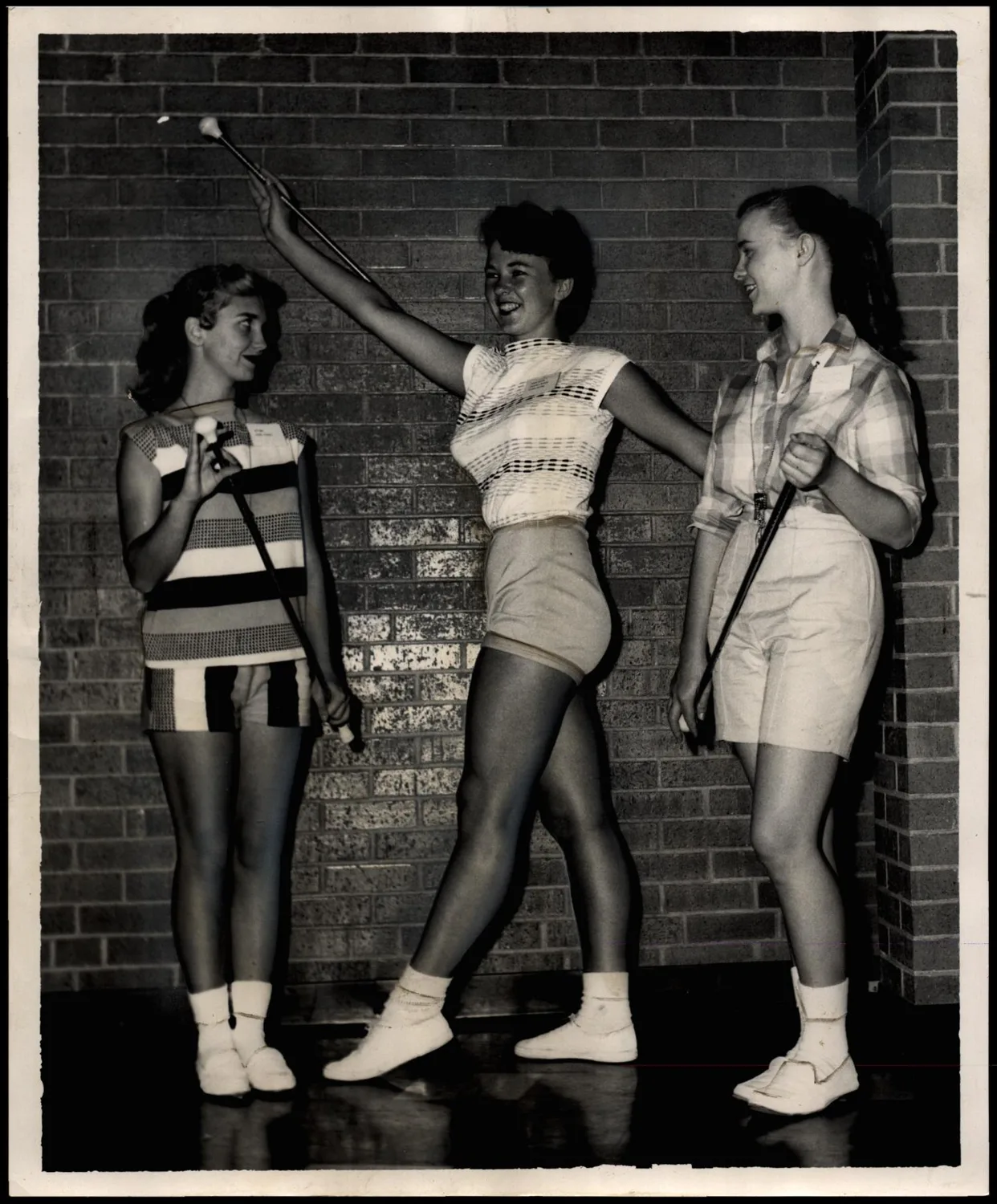 Photograph used for a story in the Oklahoma Times newspaper. Caption: "Czarina Holland, center national twirling champion from Seiling high School, demonstrates the fine points of baton handling to Kay Come, left, and Frances Chittenden both of Thomas, during the annual summer band camp on the Southwestern State College campus."