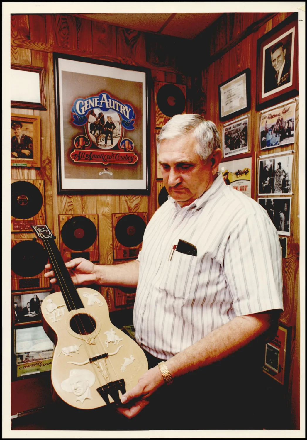 Photograph used for a story in the Daily Oklahoman newspaper. Caption: "Elvin Sweeten, director of the Gene Autry museum in Gene Autry, holds a guitar bearing the cowboy star's name."
