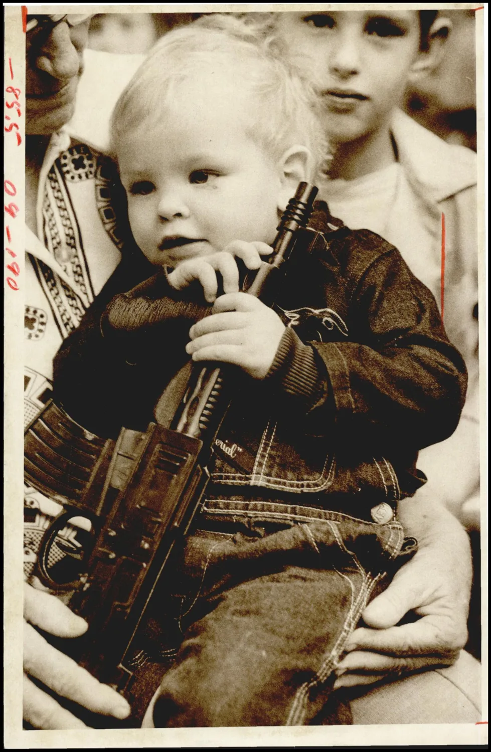 Photograph used for a story in the Oklahoma Times newspaper. Caption: "Randy Wayne Harris, 17 months old, , lower right, hugs his newly acquired toy gun during the Tuesday party, which featured the Highlander Pipers and Drum Band of Oklahoma City."